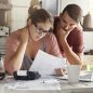 Young Caucasian family having debt problems, not able to pay out their loan. Female in glasses and brunette man studying paper form bank while managing domestic budget together in kitchen interior